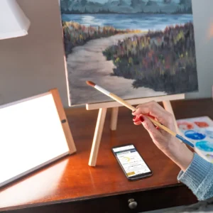 Person painting landscape on canvas with headphones.