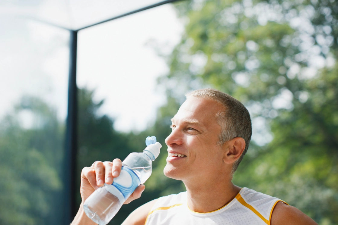 Man drinking water outdoors, smiling contentedly.